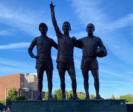 Bronze statues of George Best, Denis Law and Sir Bobby Charlton standing together outside Old Trafford